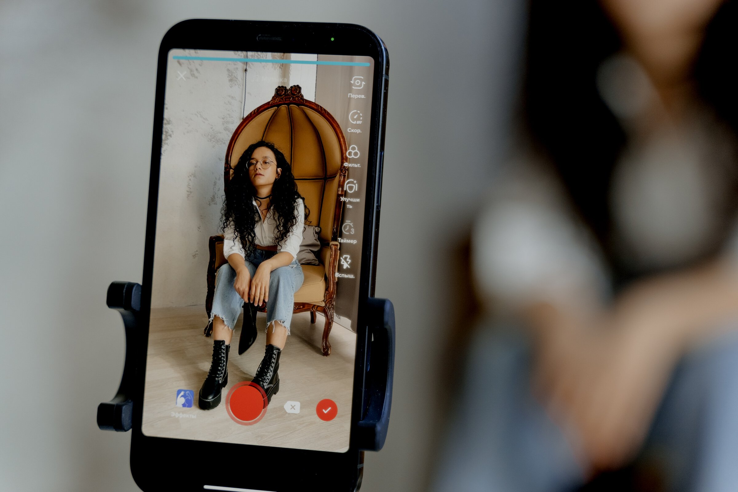 A Close-Up Shot of a Smartphone Recording a Woman Sitting on a Chair